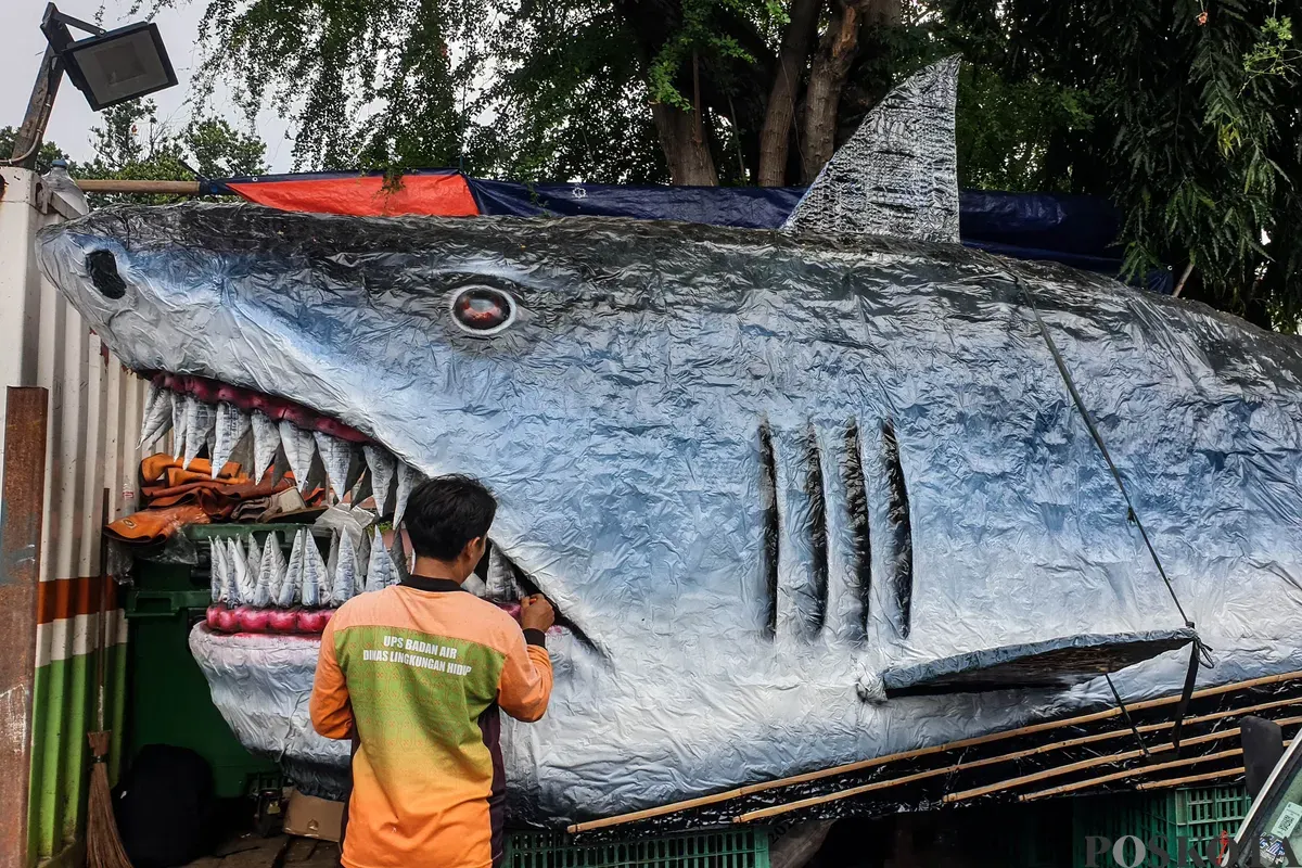 Petugas Unit Pengananan Sampah (UPS) Badan Air Kecamatan Johar Baru sibuk menyelesaikan perahu berbentuk ikan hiu di Johar Baru, Jakarta Pusat, Minggu, 21 September 2025. (Sumber: Poskota/Bilal Nugraha Ginanjar)