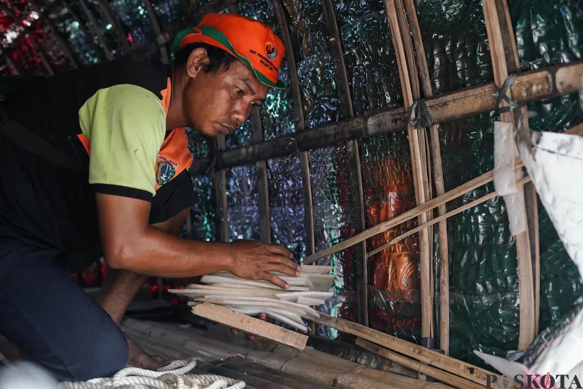 Petugas Unit Pengananan Sampah (UPS) Badan Air Kecamatan Johar Baru sibuk menyelesaikan perahu berbentuk ikan hiu di Johar Baru, Jakarta Pusat, Minggu, 21 September 2025. (Sumber: Poskota/Bilal Nugraha Ginanjar)