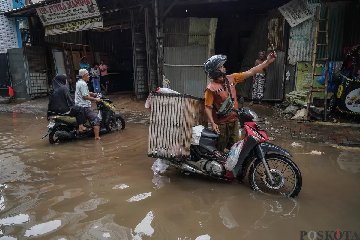 Warga melintasi genangan banjir di Jalan Swadharma Raya, Jakarta Selatan, Jumat, 20 Februari 2026. (Sumber: Poskota/Bilal Nugraha Ginanjar)