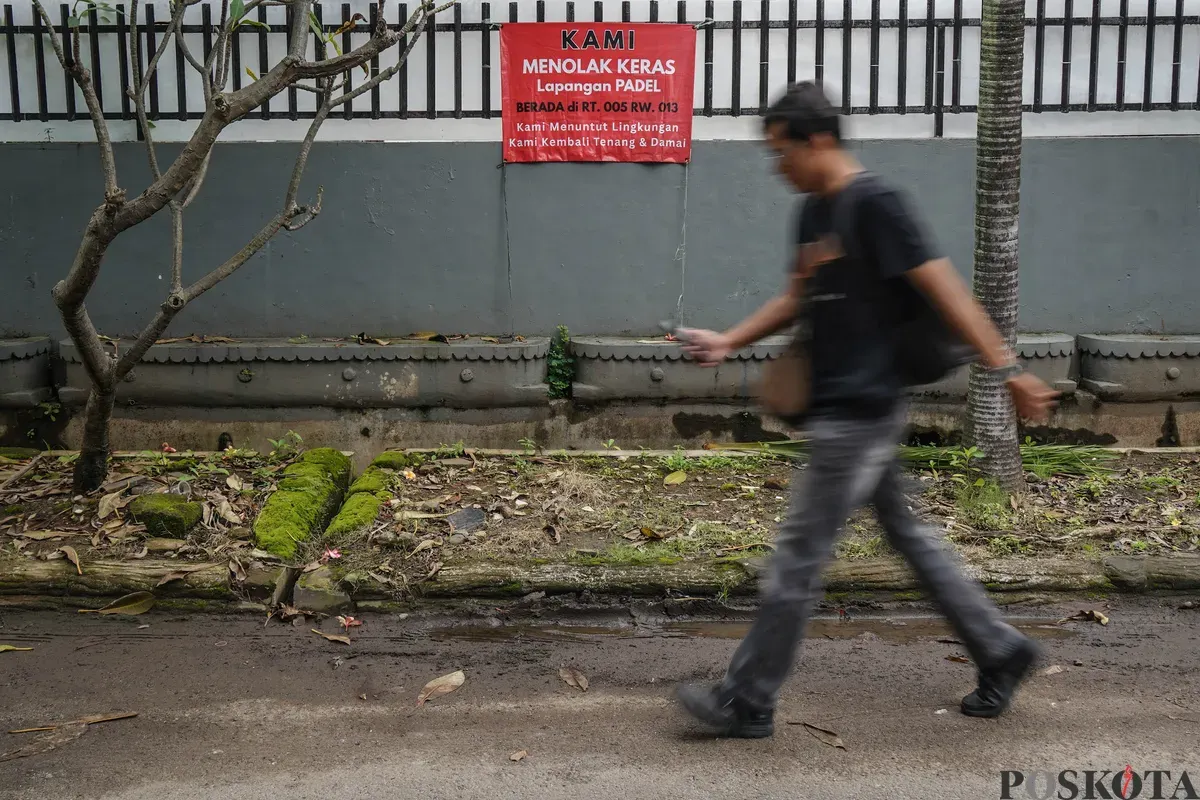 Warga berjalan melewati spanduk penolakan lapangan padel di Jalan Pulomas Barat II, Kayu Putih, Jakarta Timur, Minggu, 22 Februari 2026. (Sumber: Poskota/Bilal Nugraha Ginanjar)