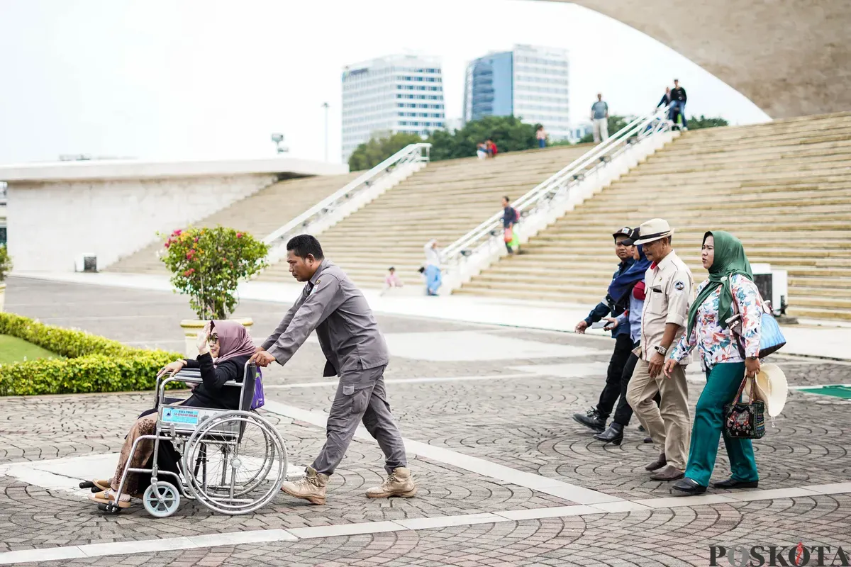 Warga membantu penyandang disabilitas menaiki lift chair atau kursi angkat di kawasan Monumen Nasional (Monas), Jakarta, Rabu, 7 Januari 2026. (Sumber: Poskota/Bilal Nugraha Ginanjar)