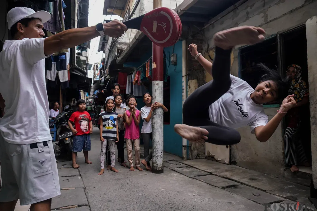 Sore itu, sorakan anak-anak terdengar ramai di sebuah gang gelap Ibu Kota. Tanpa matras profesional atau fasilitas mewah, anak-anak berlatih akrobatik mulai dari salto hingga tendangan. (Sumber: Poskota/Bilal Nugraha Ginanjar)