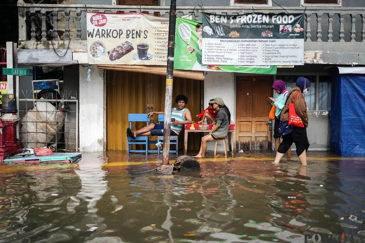 Warga berjalan melintasi banjir di Jalan Latumenten, Jelambar, Jakarta Barat, Jumat, 23 Januari 2026. (Sumber: Poskota/Bilal Nugraha Ginanjar)