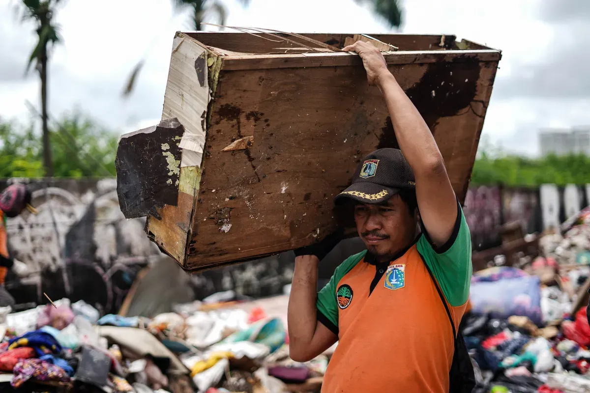 Petugas mengumpulkan sampah sisa banjir yang berasal dari wilayah permukiman kawasan Rawa Buaya di Jalan Inspeksi Kali Mookervart, Daan Mogot, Jakarta, Senin, 26 Januari 2026. (Sumber: Poskota/Bilal Nugraha Ginanjar)
