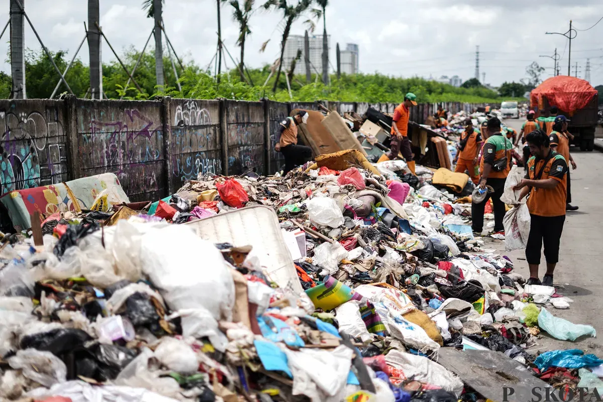 Petugas mengumpulkan sampah sisa banjir yang berasal dari wilayah permukiman kawasan Rawa Buaya di Jalan Inspeksi Kali Mookervart, Daan Mogot, Jakarta, Senin, 26 Januari 2026. (Sumber: Poskota/Bilal Nugraha Ginanjar)