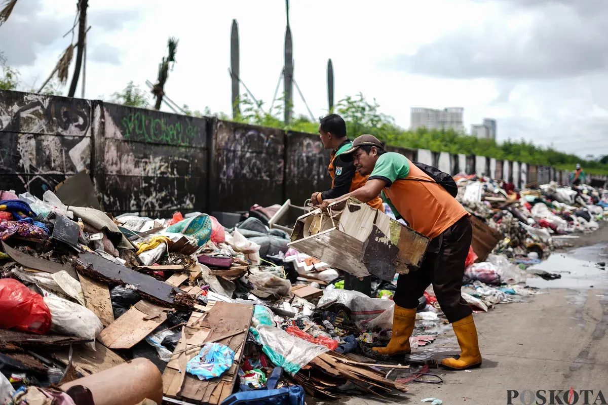 Petugas mengumpulkan sampah sisa banjir yang berasal dari wilayah permukiman kawasan Rawa Buaya di Jalan Inspeksi Kali Mookervart, Daan Mogot, Jakarta, Senin, 26 Januari 2026. (Sumber: Poskota/Bilal Nugraha Ginanjar)