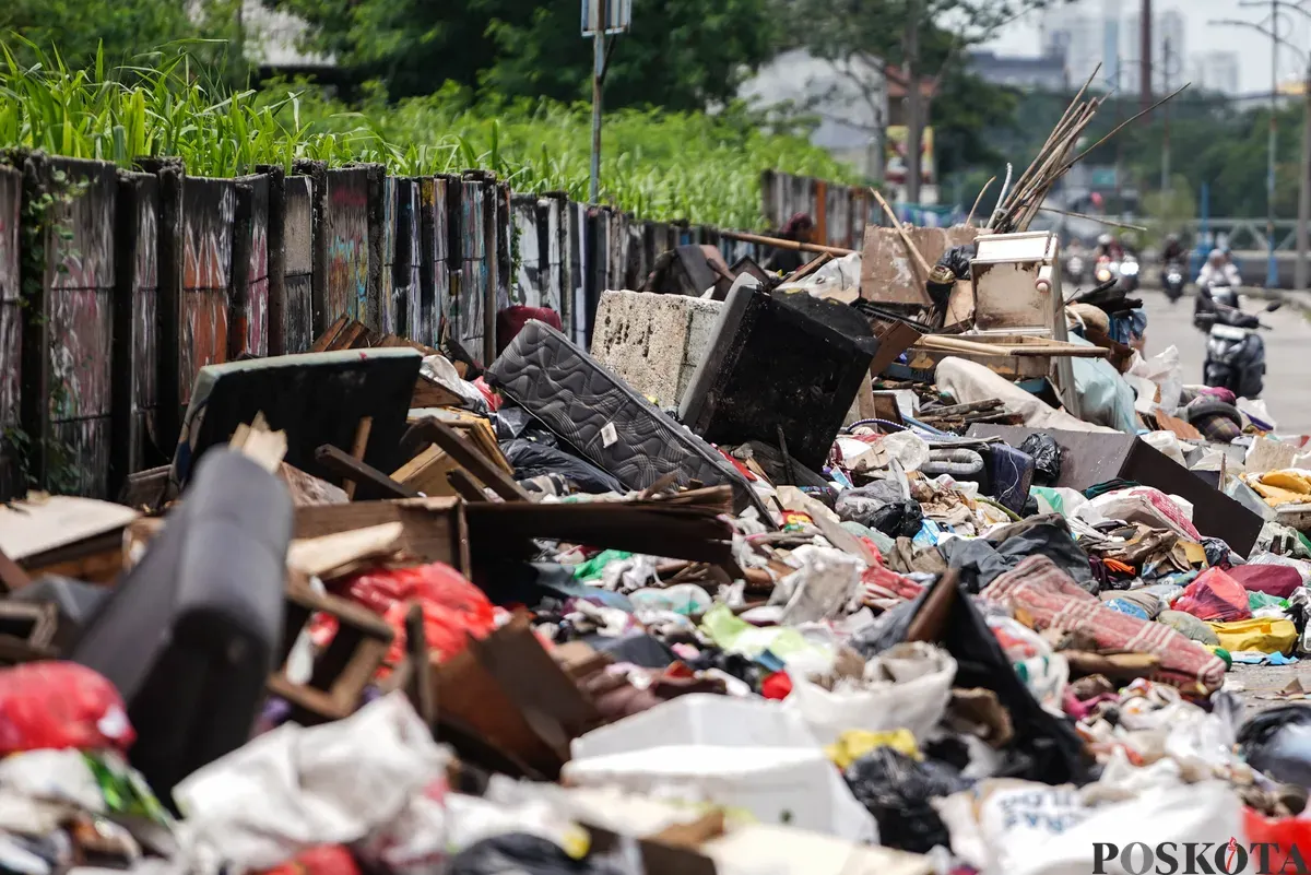 Petugas mengumpulkan sampah sisa banjir yang berasal dari wilayah permukiman kawasan Rawa Buaya di Jalan Inspeksi Kali Mookervart, Daan Mogot, Jakarta, Senin, 26 Januari 2026. (Sumber: Poskota/Bilal Nugraha Ginanjar)