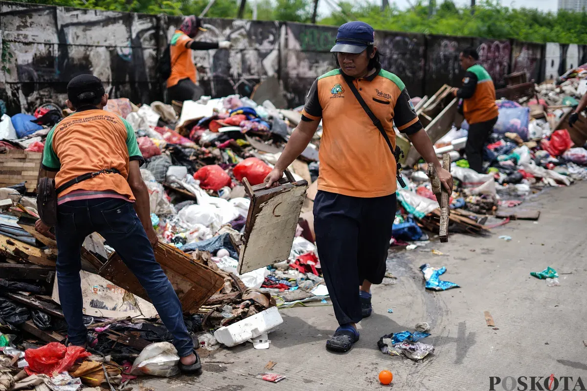 Petugas mengumpulkan sampah sisa banjir yang berasal dari wilayah permukiman kawasan Rawa Buaya di Jalan Inspeksi Kali Mookervart, Daan Mogot, Jakarta, Senin, 26 Januari 2026. (Sumber: Poskota/Bilal Nugraha Ginanjar)