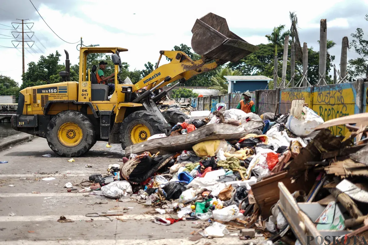Petugas mengumpulkan sampah sisa banjir yang berasal dari wilayah permukiman kawasan Rawa Buaya di Jalan Inspeksi Kali Mookervart, Daan Mogot, Jakarta, Senin, 26 Januari 2026. (Sumber: Poskota/Bilal Nugraha Ginanjar)