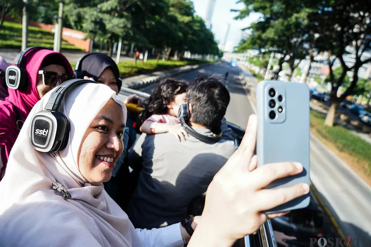 Pengunjung menikmati suasana bersama keluarga sambil berswafoto dengan latar belakang kota dari bagian atap bus wisata Open Top Tour of Jakarta, Jumat, 4 April 2025. (Sumber: Poskota/Bilal Nugraha Ginanjar)
