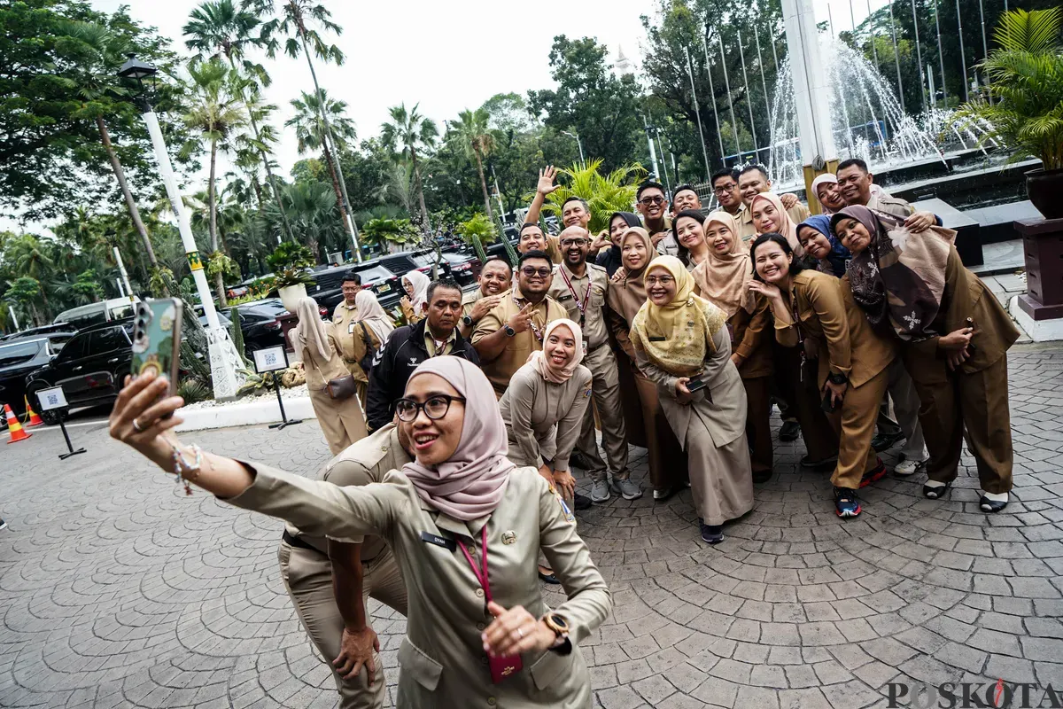 Sejumlah ASN Pemerintah Provinsi DKI Jakarta berswafoto bersama di halaman Balai Kota Jakarta pada hari pertama masuk kerja usai libur Lebaran 2025. (Sumber: Poskota/Bilal Nugraha Ginanjar)
