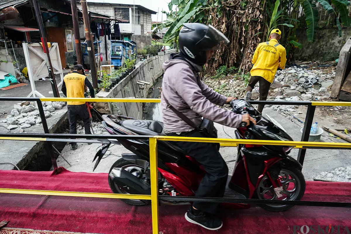 Warga melintas di jembatan sementara menggunakan sepeda motor di Jalan Kesatriaan X, Kebon Manggis, Matraman, Jakarta Timur, Kamis, 10 April 2025. (Sumber: Poskota/Bilal Nugraha Ginanjar)