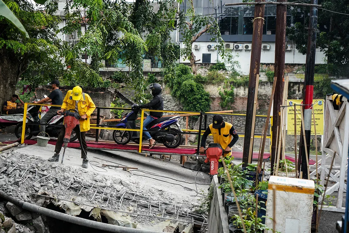 Warga melintas di jembatan sementara menggunakan sepeda motor di Jalan Kesatriaan X, Kebon Manggis, Matraman, Jakarta Timur, Kamis, 10 April 2025. (Sumber: Poskota/Bilal Nugraha Ginanjar)