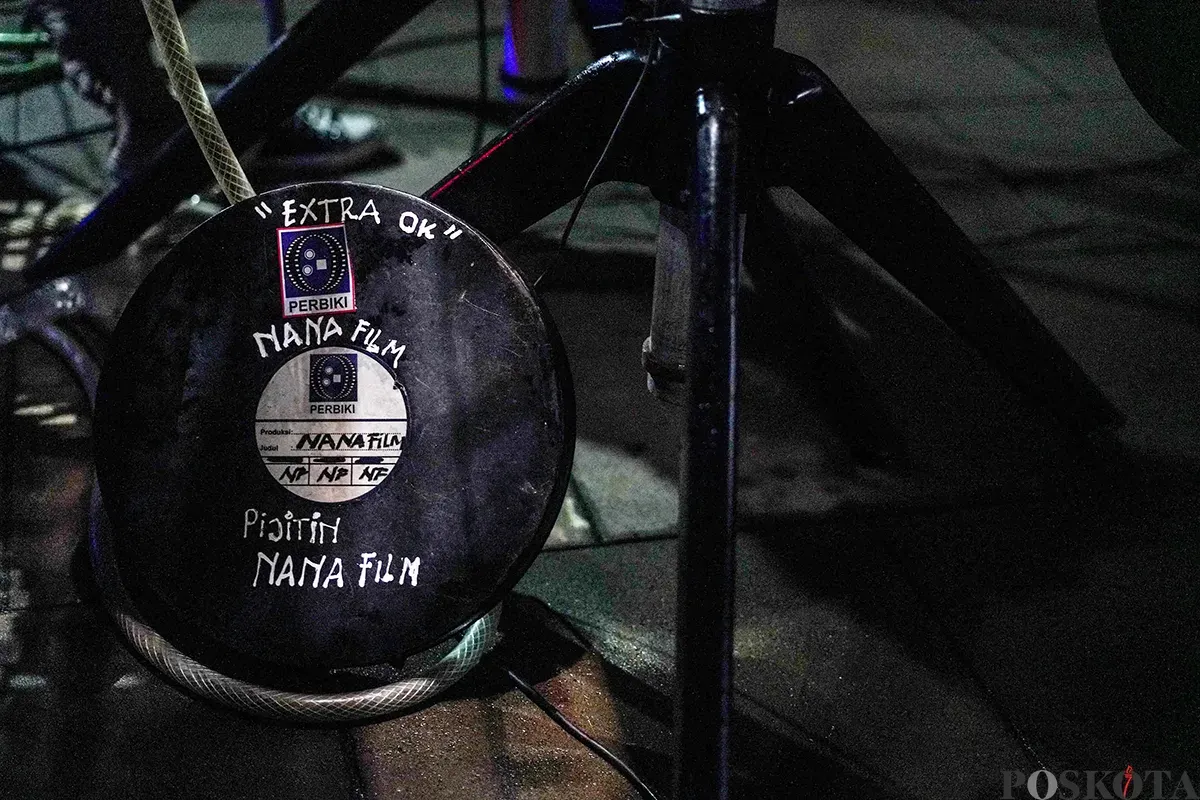 Operator film layar tancap memutarkan rol film era menggunakan mesin proyektor di Waduk Lebak Bulus, Jakarta Selatan, Jum'at, 18 April 2025. (Sumber: Poskota/Bilal Nugraha Ginanjar)