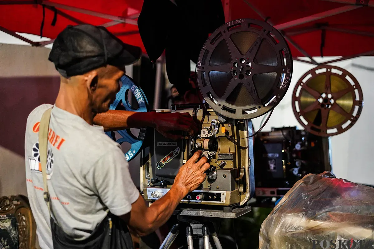 Operator film layar tancap memutarkan rol film era menggunakan mesin proyektor di Waduk Lebak Bulus, Jakarta Selatan, Jum'at, 18 April 2025. (Sumber: Poskota/Bilal Nugraha Ginanjar)