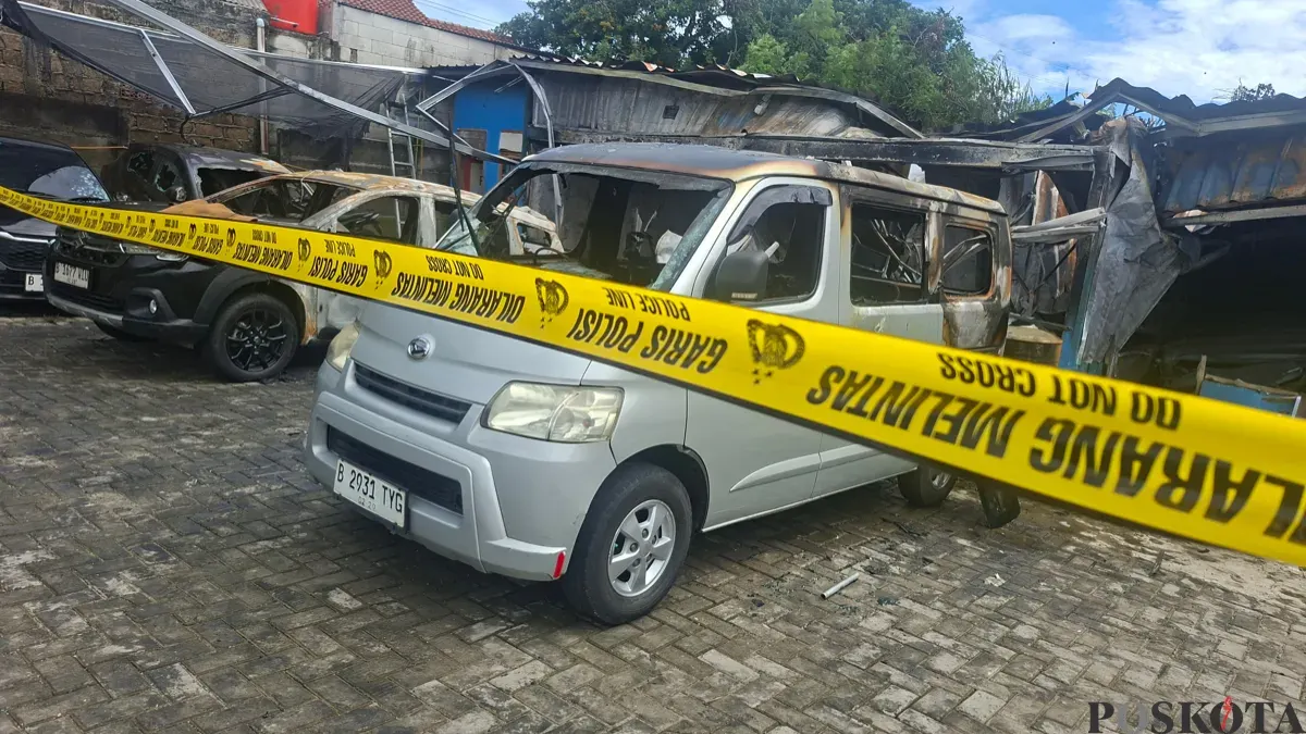 Kondisi terkini bangunan kantor rental dan bengkel oli terbakar. Terlihat sisa bangkai empat unit mobil rental dan satu motor yang terbakar dan dipasang garis polisi. (Sumber: Poskota/Angga Pahlevi)