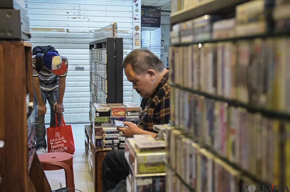 Pengunjung sekaligus penikmat koleksi barang lawas, melihat dan menilik kaset pita yang jaya pada era 80 hingga 90-an di satu di antara lapak penjual kaset di Blok M Square, Jakarta, Senin, 20 Januari 2025. (Sumber: Poskoata/ Bilal Nugraha Ginanjar)