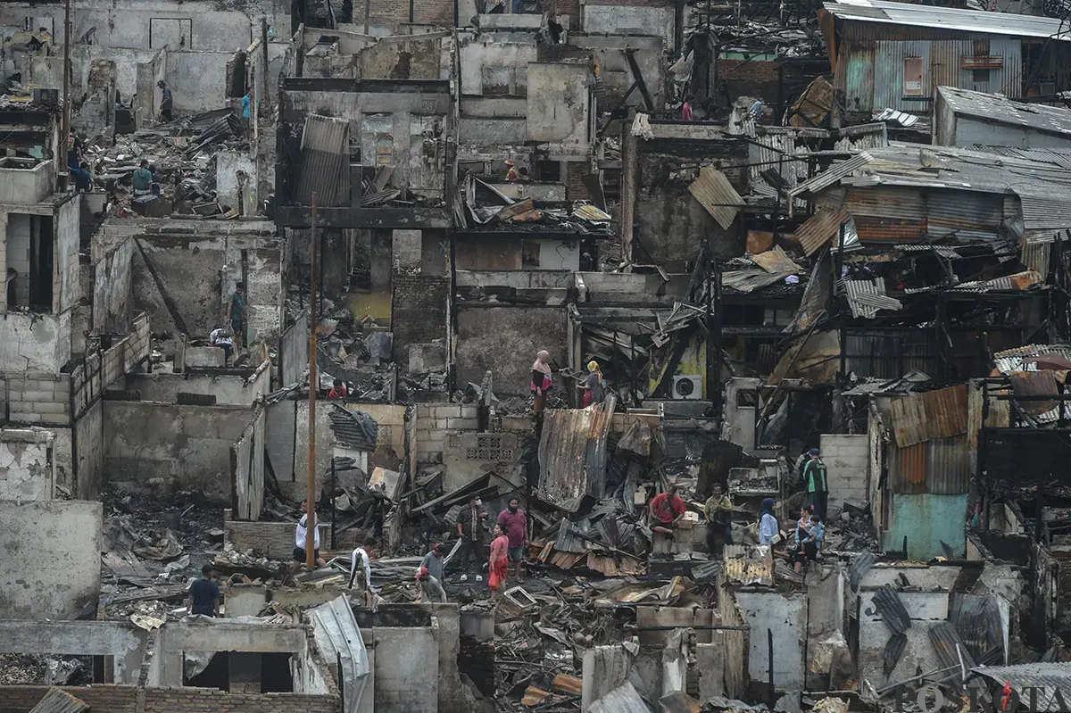 Sejumlah warga menyaksikan proses pendinginan terhadap puing-puing rumah yang terbakar yang dilakukan oleh petugas pemadam kebakaran usai terjadi musibah kebakaran di permukiman padat penduduk di Jalan Kemayoran Gempol, Kemayoran, Jakarta, Selasa, 21 Januari 2025. (Sumber: Poskota/ Bilal Nugraha Ginanjar)