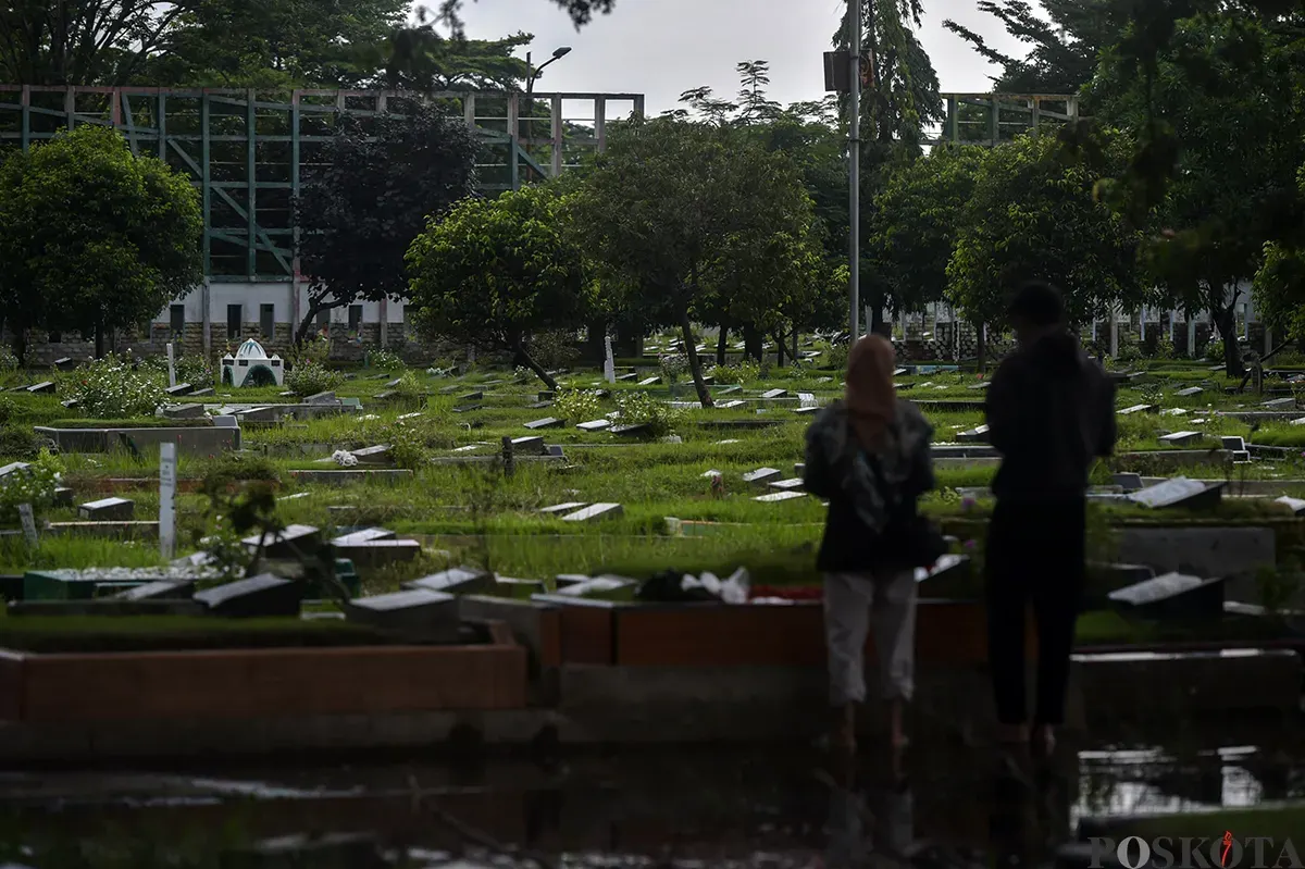 Warga berdoa di makam kerabat yang terendam air di Tempat Pemakaman Umum (TPU) Semper, Cilincing, Jakarta Utara, Jumat, 24 Januari, 2025. (Sumber: Poskota/Bilal Nugraha Ginanjar)