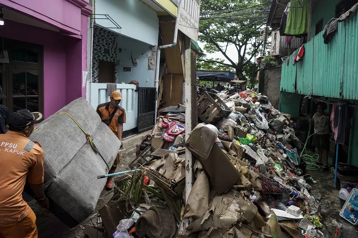Petugas Penanganan Prasarana dan Sarana Umum (PPSU) Kelurahan Kapuk, mengangkut tumpukan sisa sampah yang terbawa arus air banjir di area gang permukiman pada penduduk di kawasan Jalan Kapuk Bongkaran, Cengkareng, Jakarta Barat, Kamis, 30 Januari 2025. (Sumber: Poskota/ Bilal Nugraha Ginanjar)