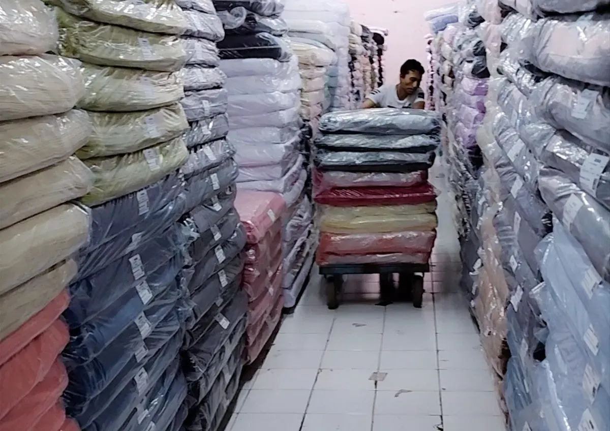 Pekerja Focus Textile mendorong tumpukan kain yang dikemas rapi di salah satu gudang. Industri tekstil tetap beroperasi di tengah tekanan ekonomi dan persaingan impor. (Sumber: Istimewa)