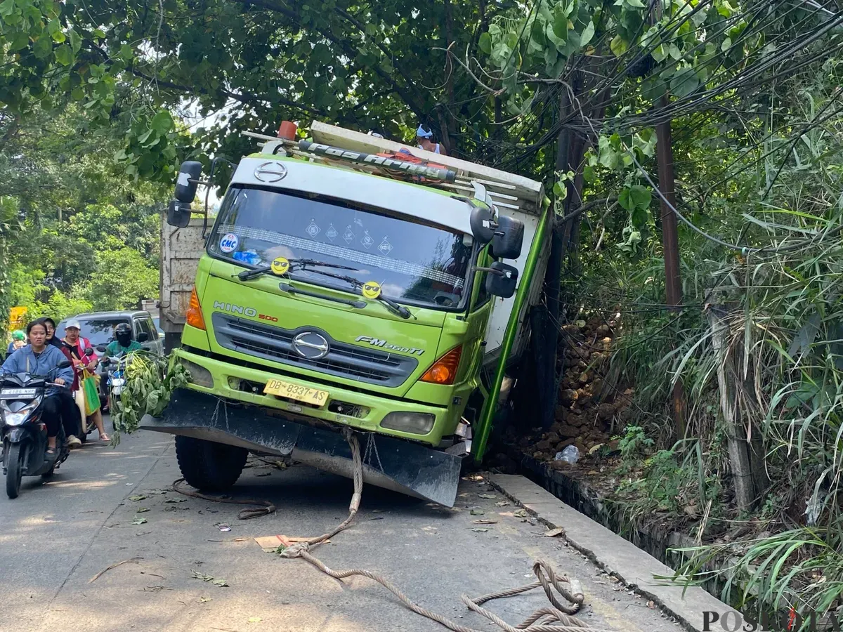 Truk Hino berwarna hijau-putih terperosok ke parit setelah gagal menanjak di Tanjakan Parakan, Pamulang, Tangerang Selatan, pada Jumat, 4 Juli 2025. (Sumber: Poskota/Primayanti Juli Kumala Manalu)