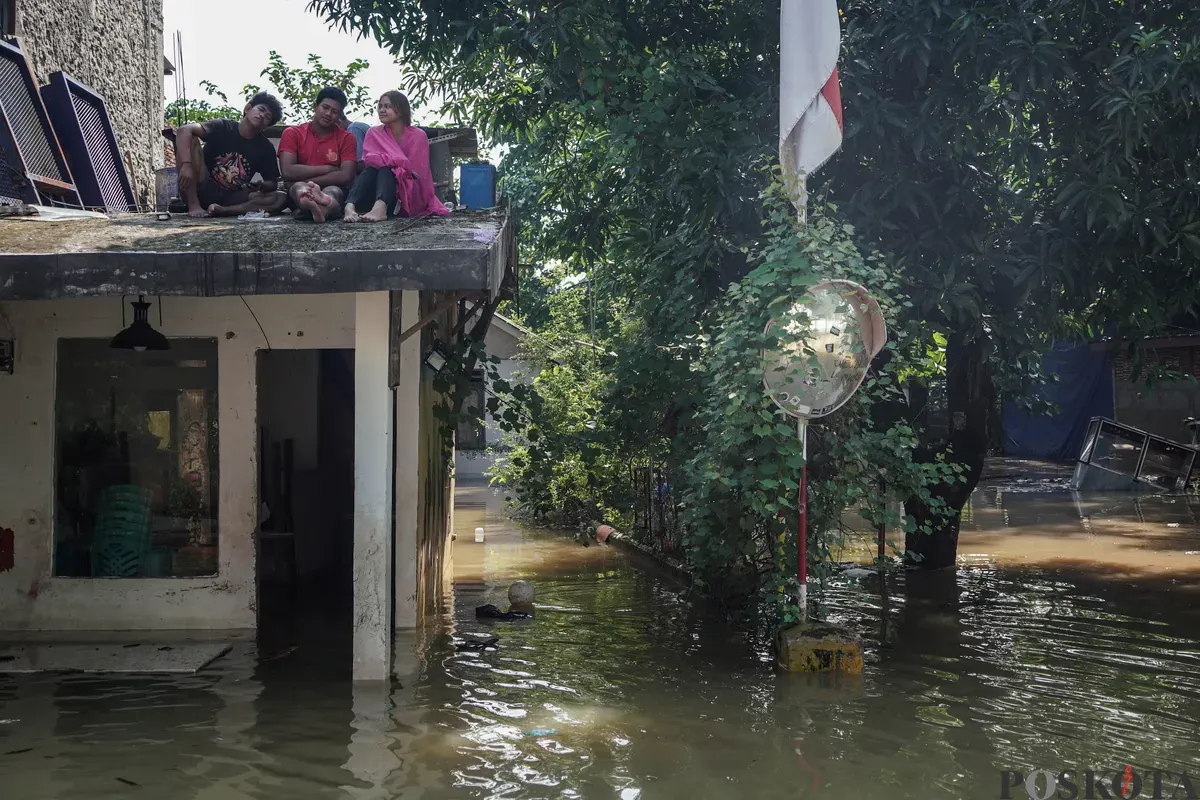 Warga duduk diatas rumah yang tergenang banjir di Jalan Pirus, Bidara Cina, Jatinegara, Jakarta Timur, Minggu, 8 Juli 2025. (Sumber: Poskota/Bilal Nugraha Ginanjar)