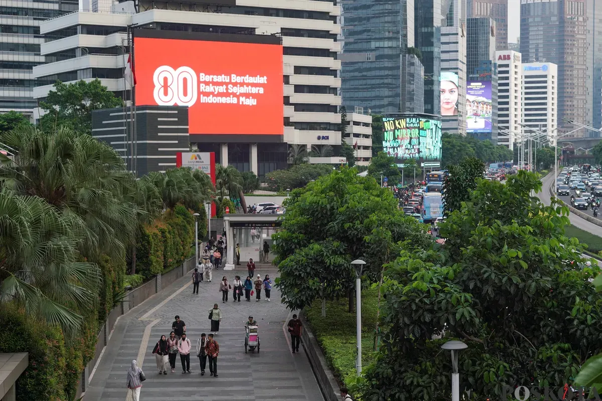 Sejumlah warga melintas di dekat Videotron yang menampilkan logo HUT RI ke-80 di kawasan Jalan Sudirman, Jakarta, Kamis, 24 Juli 2025. (Sumber: Poskota/Bilal Nugraha Ginanjar)