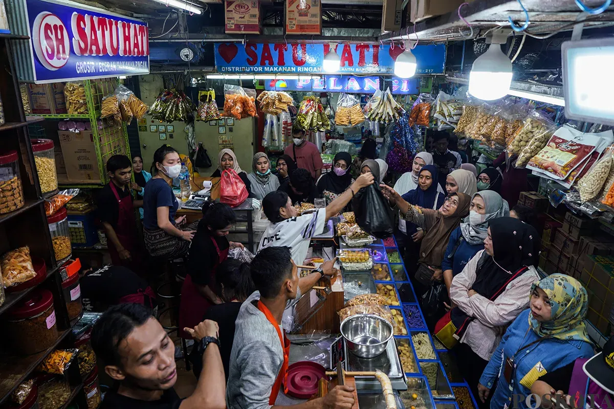 Pedagang melayani sejumlah pembeli aneka rasa kue kering yang ditawarkan di lapaknya di Pasar Jatinegara, Jakarta Timur, Jumat, 21 Maret 2025. (Sumber: Poskota/Bilal Nugraha Ginanjar)