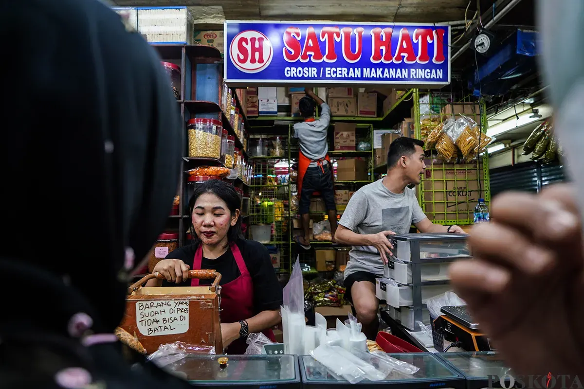 Pedagang melayani sejumlah pembeli aneka rasa kue kering yang ditawarkan di lapaknya di Pasar Jatinegara, Jakarta Timur, Jumat, 21 Maret 2025. (Sumber: Poskota/Bilal Nugraha Ginanjar)