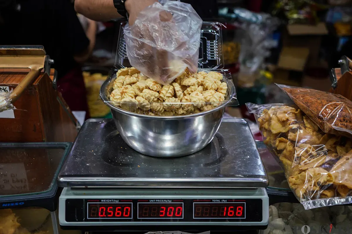 Pedagang melayani sejumlah pembeli aneka rasa kue kering yang ditawarkan di lapaknya di Pasar Jatinegara, Jakarta Timur, Jumat, 21 Maret 2025. (Sumber: Poskota/Bilal Nugraha Ginanjar)