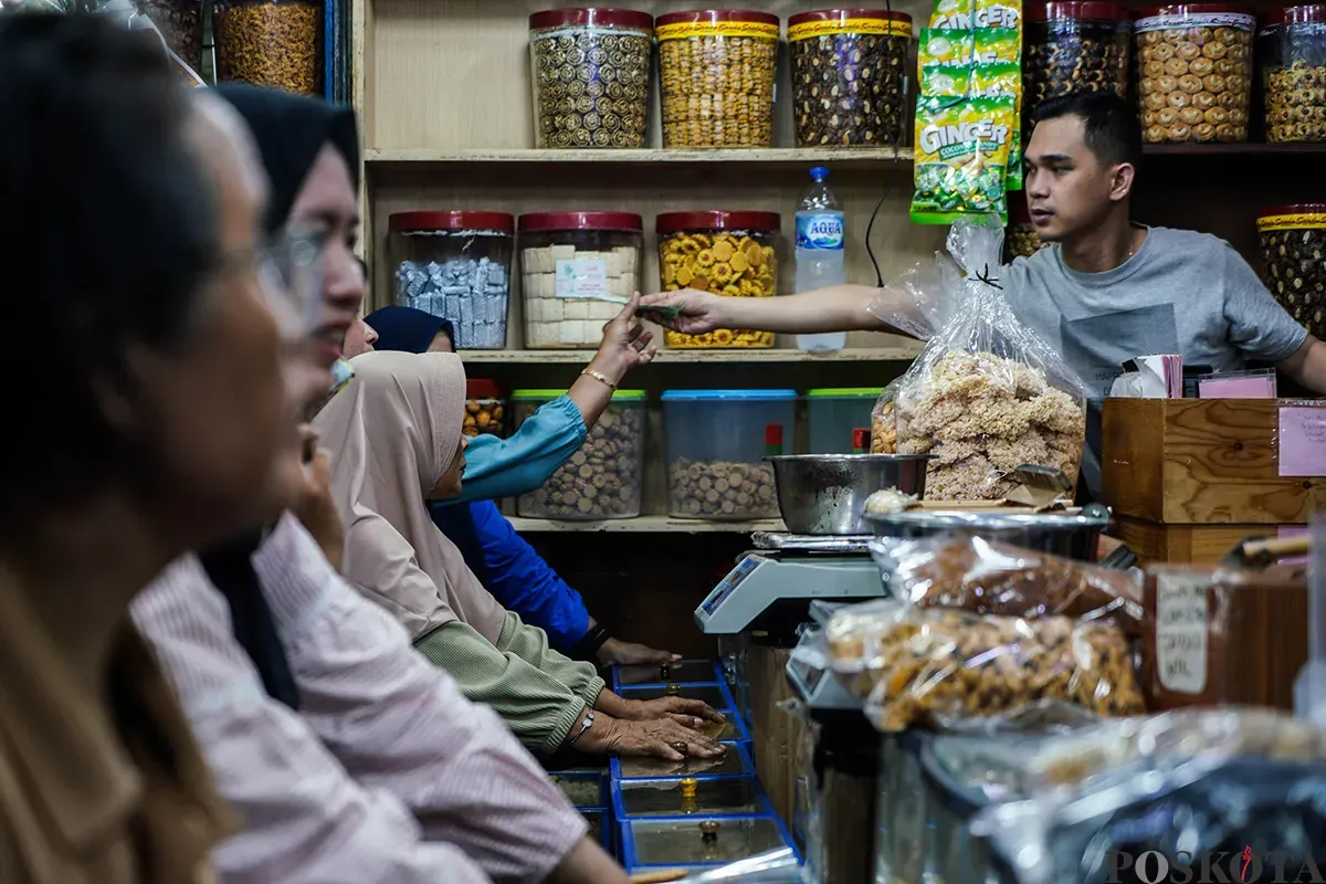 Pedagang melayani sejumlah pembeli aneka rasa kue kering yang ditawarkan di lapaknya di Pasar Jatinegara, Jakarta Timur, Jumat, 21 Maret 2025. (Sumber: Poskota/Bilal Nugraha Ginanjar)