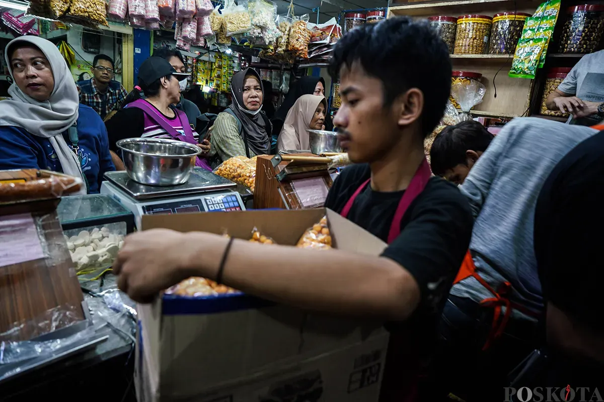 Pedagang melayani sejumlah pembeli aneka rasa kue kering yang ditawarkan di lapaknya di Pasar Jatinegara, Jakarta Timur, Jumat, 21 Maret 2025. (Sumber: Poskota/Bilal Nugraha Ginanjar)