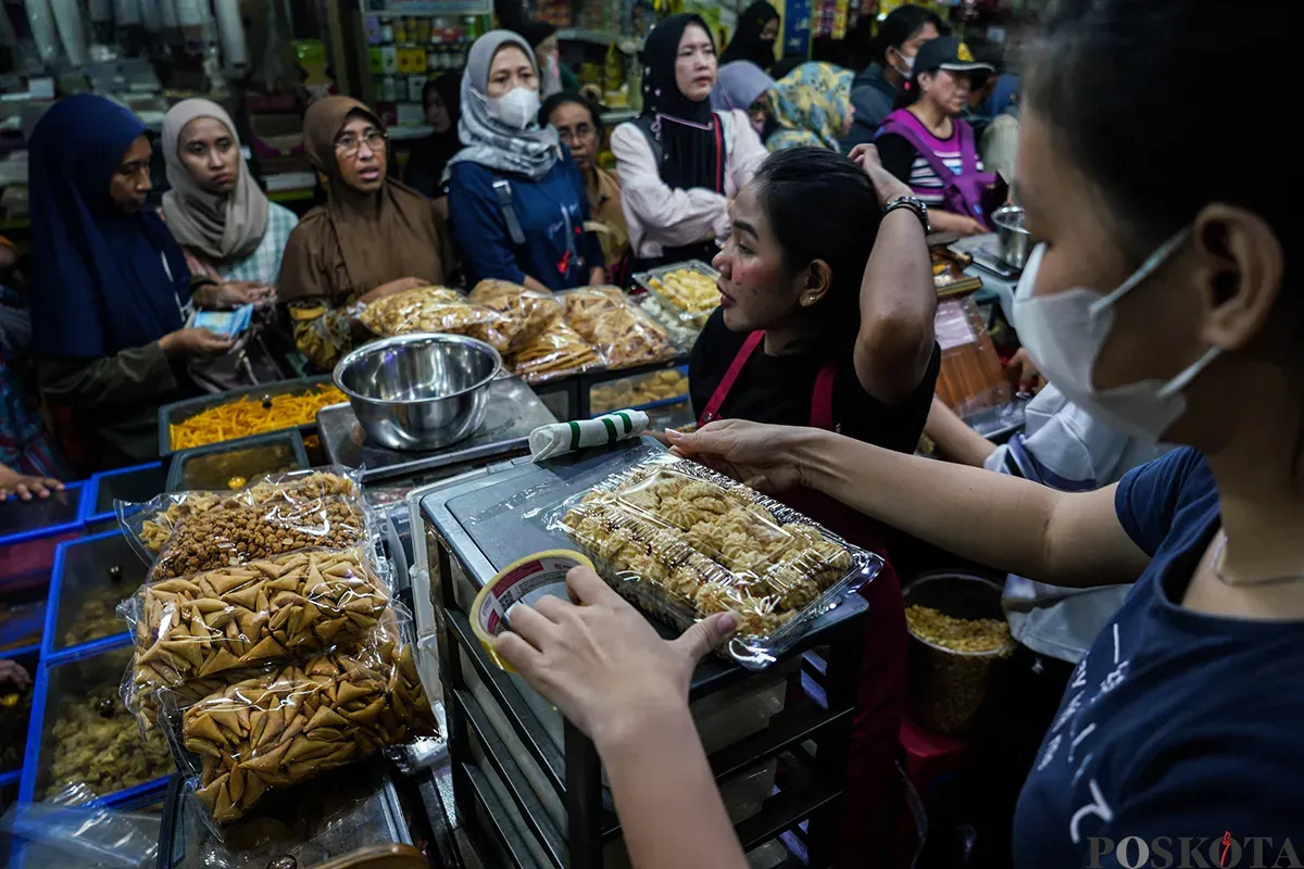 Pedagang melayani sejumlah pembeli aneka rasa kue kering yang ditawarkan di lapaknya di Pasar Jatinegara, Jakarta Timur, Jumat, 21 Maret 2025. (Sumber: Poskota/Bilal Nugraha Ginanjar)