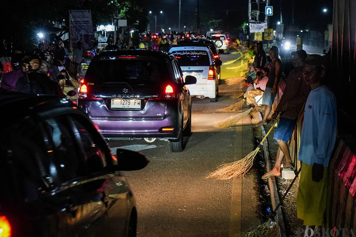 Sejumlah warga menggunakan sapu untuk mengambil uang sedekah yang dilempar para pengendara mudik di Jalur Pantura Sukra, Indramayu, Jawa Barat, Jumat, 28 Maret 2025. (Sumber: Poskoata/ Bilal Nugraha Ginanjar)