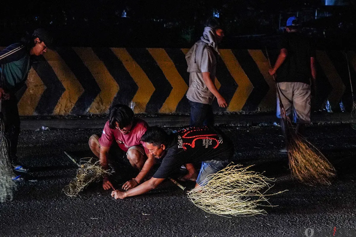Sejumlah warga menggunakan sapu untuk mengambil uang sedekah yang dilempar para pengendara mudik di Jalur Pantura Sukra, Indramayu, Jawa Barat, Jumat, 28 Maret 2025. (Sumber: Poskoata/ Bilal Nugraha Ginanjar)