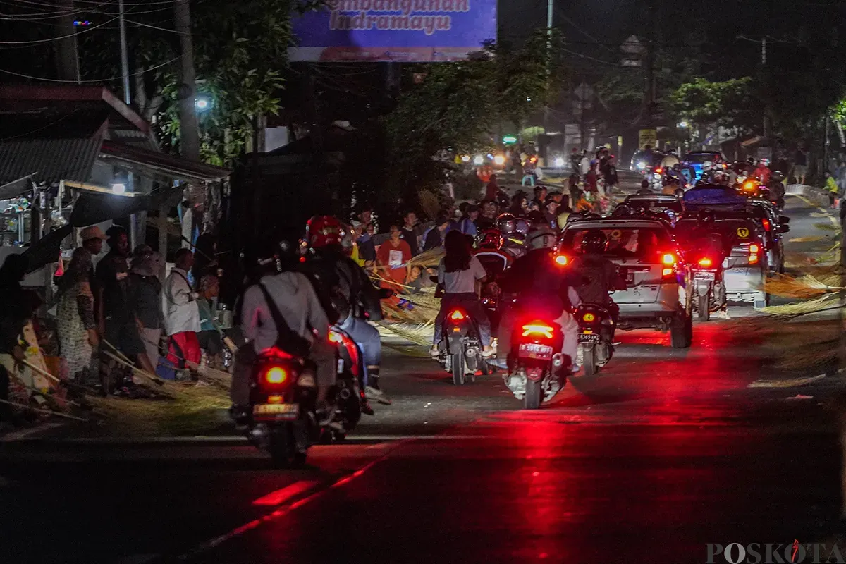 Sejumlah warga menggunakan sapu untuk mengambil uang sedekah yang dilempar para pengendara mudik di Jalur Pantura Sukra, Indramayu, Jawa Barat, Jumat, 28 Maret 2025. (Sumber: Poskoata/ Bilal Nugraha Ginanjar)