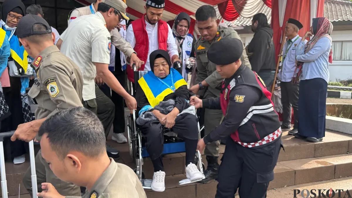 Petugas haji dan Satpol PP membantu jemaah haji lanjut usia menuruni tangga Gedung Tegar Beriman, Cibinong saat pelepasan kloter pertama Kabupaten Bogor, Kamis 23 April 2026. (Sumber: Poskota/Giffar Rivana)