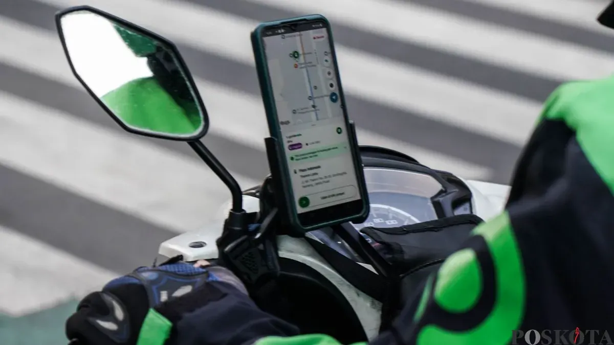 Driver ojol menggunakan ponsel di pinggir jalan saat menunggu orderan, ilustrasi pentingnya perangkat andal di tengah mobilitas tinggi. (Sumber: Poskota/Bilal Nugraha Ginanjar)