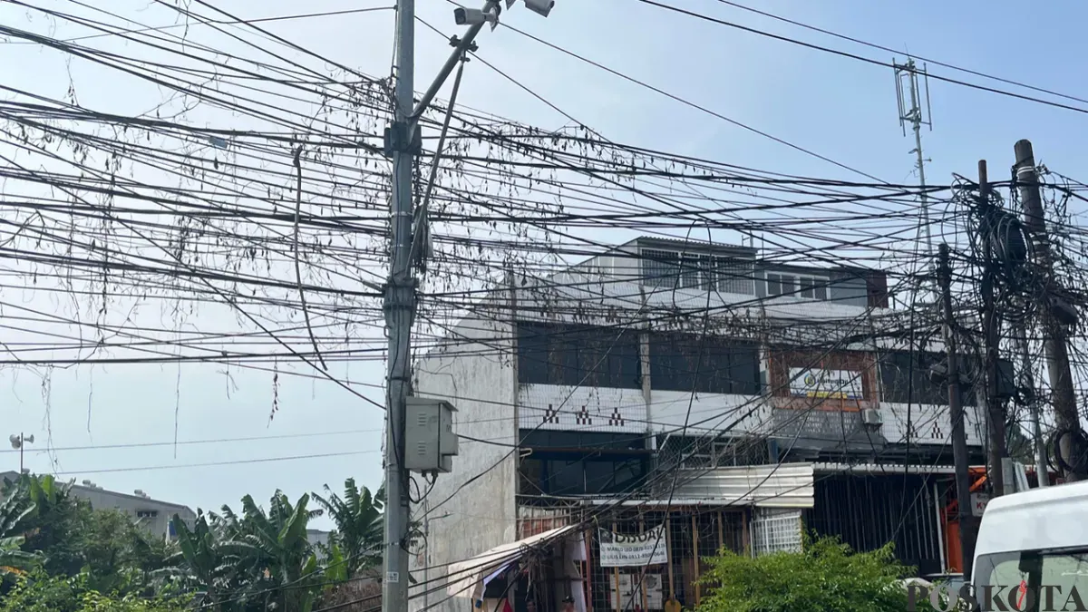 Warga sedang membenahi kabel menjuntai akibat tersenggol truk besar di Jalan Peta Selatan dan Jalan Peta Barat, Kalideres, Jakarta Barat, Selasa 23 Juni 2026. (Sumber: Poskota/Pandi Ramedhan)