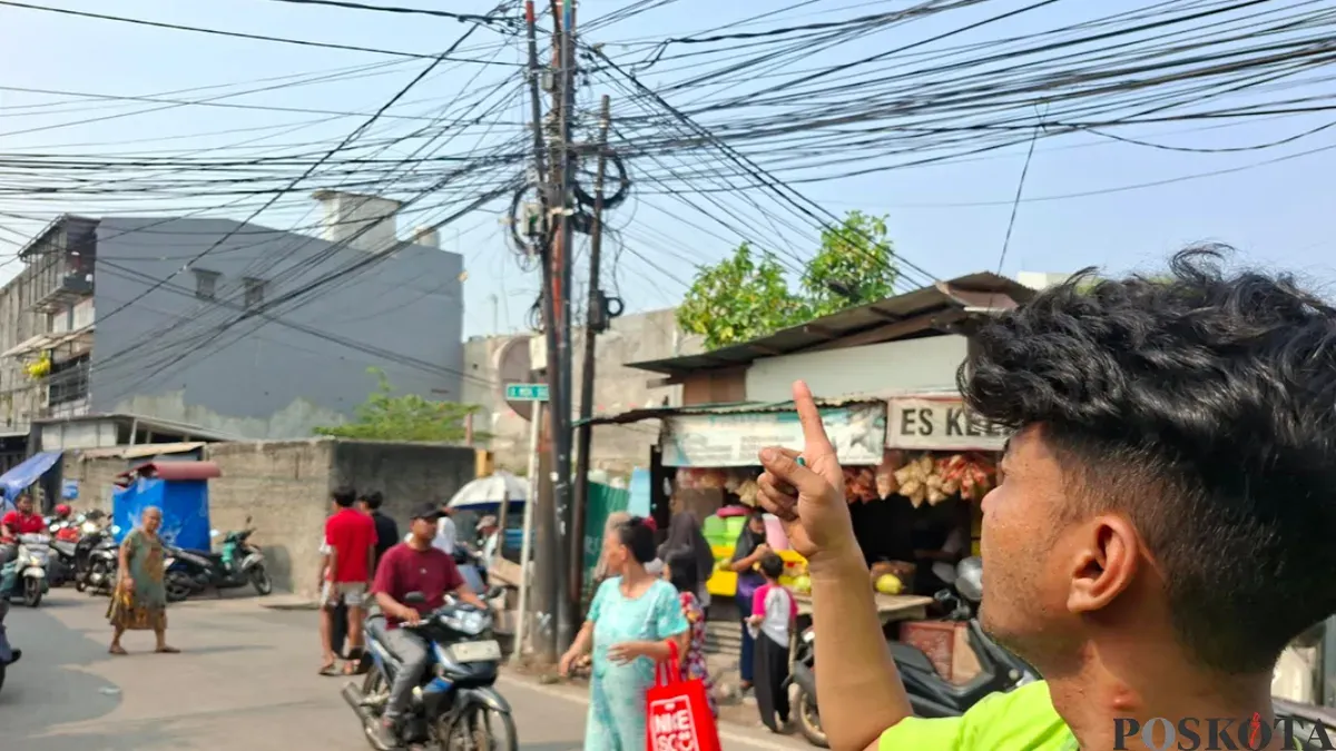 Ketua RT 14 RW 005, Rifki Ramadhan menunjukan lokasi tiang listrik kabel semerawut yang berada di pinggir Jalan Kramat Pulo Dalam. (Sumber: Poskota/Angga)