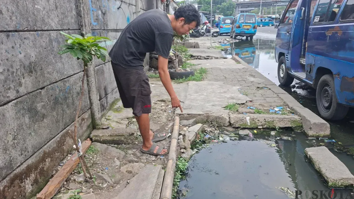 Rahmat, warga RT 07 RW 19 menunjukan luapan air got yang berasal dari lubang gorong-gorong yang terbuka di Jalan Naming Botin Kelurahan Depok, Kecamatan Pancoran Mas, Kota Depok, Selasa siang, 13 Oktober 2026. (Sumber: Poskota/Angga)