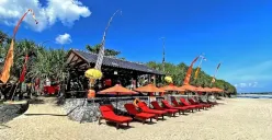 Deretan kursi panjang berwarna merah dengan payung oranye berjajar rapi di atas pasir Pantai Karang Papak, Garut. Nuansa Bali semakin terasa dengan hiasan kain poleng dan umbul-umbul di sekitar area. (Sumber: Villa&Cafe Villa Rahayu Karangpapak)