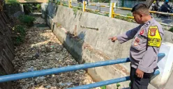 Anggota Bhabinkamtibmas Kelurahan Krukut Aiptu Andriyanto menunjukan lokasi sampah menutup aliran Kali Irigasi RW 03, Jalan Raya Krukut, Limo, Kota Depok, Senin, 13 Juli 2026. (Sumber: Poskota/Angga Pahlevi)