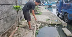 Rahmat, warga RT 07 RW 19 menunjukan luapan air got yang berasal dari lubang gorong-gorong yang terbuka di Jalan Naming Botin Kelurahan Depok, Kecamatan Pancoran Mas, Kota Depok, Selasa siang, 13 Oktober 2026. (Sumber: Poskota/Angga)