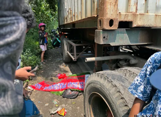 Jenazah siswa SMP yang tewas tertabrak truk petikemas di Jalan Cakung–Cilincing (Cacing), Jakarta Timur, ditutupi spanduk sebelum dievakuasi petugas. (Sumber: Poskota/M. Tegar Jihad)