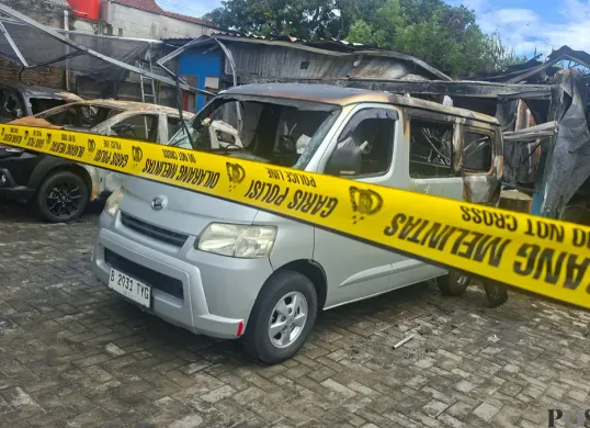 Kondisi terkini bangunan kantor rental dan bengkel oli terbakar. Terlihat sisa bangkai empat unit mobil rental dan satu motor yang terbakar dan dipasang garis polisi. (Sumber: Poskota/Angga Pahlevi)