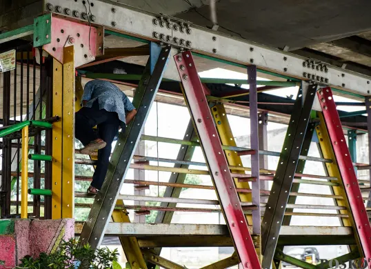 Warga berupaya menerobos pagar besi penutup dengan cara memanjat di Jembatan Penyebrangan Orang (JPO) Kolong Flyover Kalibata, Jakarta Selatan. (Sumber: Poskota/Bilal Nugraha Ginanjar)