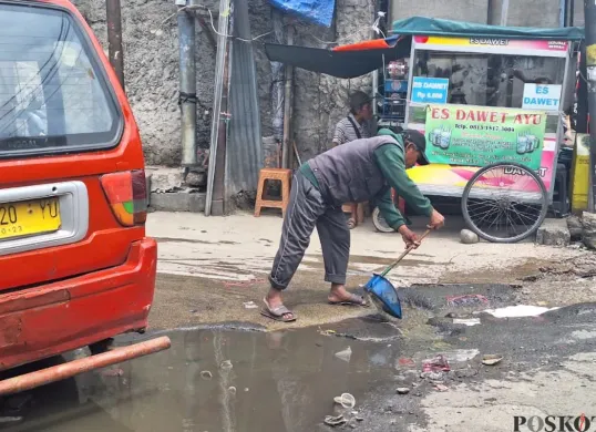Warga membersihkan genangan air di area Stasiun Bekasi menuju Kampung Pintu, Jalan Raya Perjuangan, Bekasi Utara, Kota Bekasi, Rabu, 22 Januari 2025. (Sumber: Poskota/Ihsan Fahmi)