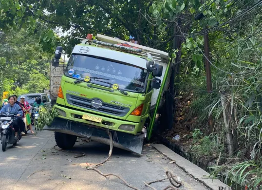 Truk Hino berwarna hijau-putih terperosok ke parit setelah gagal menanjak di Tanjakan Parakan, Pamulang, Tangerang Selatan, pada Jumat, 4 Juli 2025. (Sumber: Poskota/Primayanti Juli Kumala Manalu)
